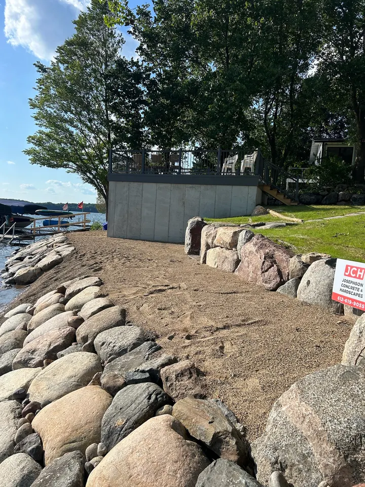 Fresh boulder riprap along a lakeshore with a graded bank and a small lake shed above