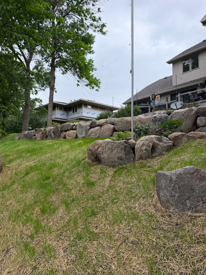 Boulder retaining wall along a seeded slope above a lakeside home, with straw covering the new seed