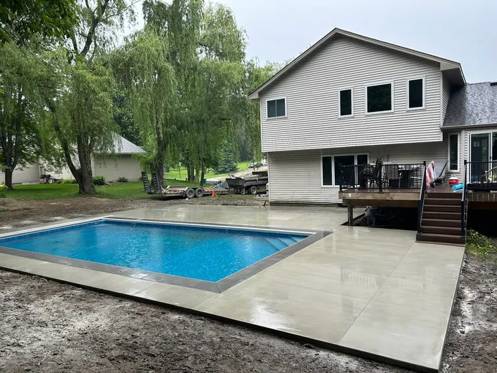 Broom-finish concrete pool deck poured around a new pool behind a two-story home