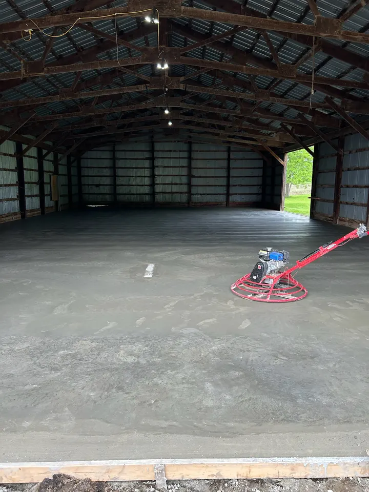 Inside a steel pole building with fresh concrete floor being finished by a power trowel