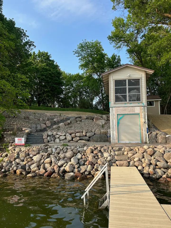 Fieldstone shoreline and boulder wall in front of a lakeside boathouse and dock