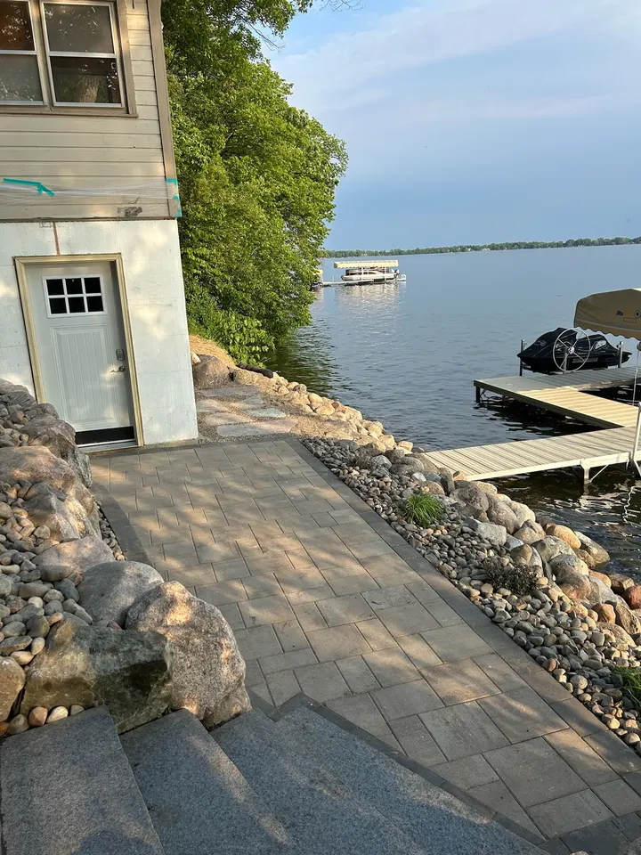 Stone steps and a paver landing leading down to a dock, with boulders along the shoreline