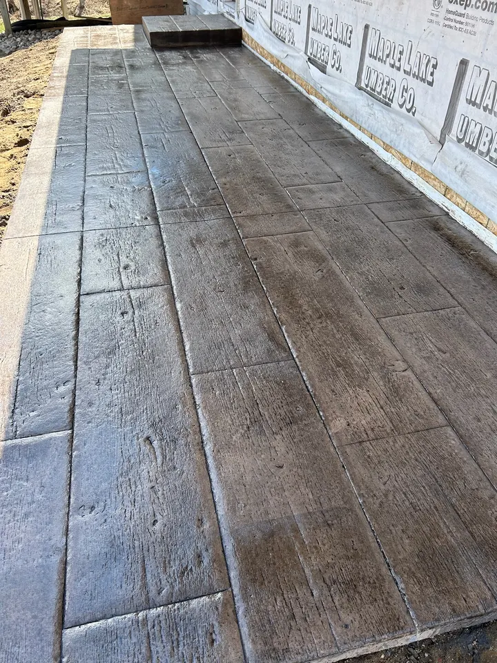 Close view of stamped concrete with a wood-plank pattern and brown stain, still wet from sealing